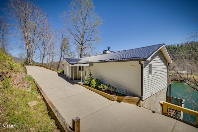 view of property exterior with a water view, metal roof, and a chimney