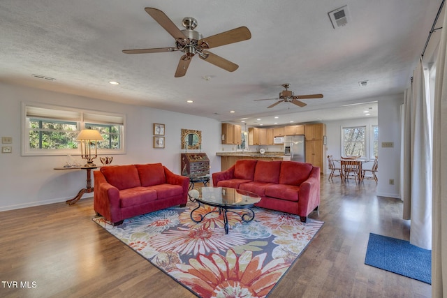 living room featuring baseboards, visible vents, wood finished floors, a textured ceiling, and recessed lighting