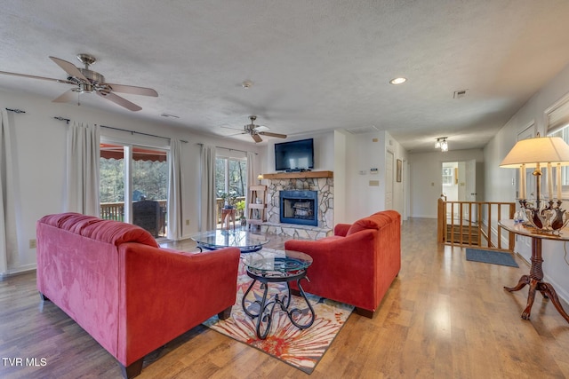 living room with a textured ceiling, a fireplace, wood finished floors, visible vents, and baseboards