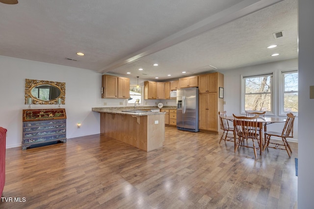 kitchen with stainless steel fridge, visible vents, a breakfast bar, a peninsula, and light wood-type flooring