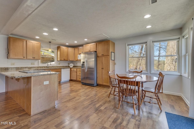 kitchen with a peninsula, white appliances, light stone counters, and light wood finished floors