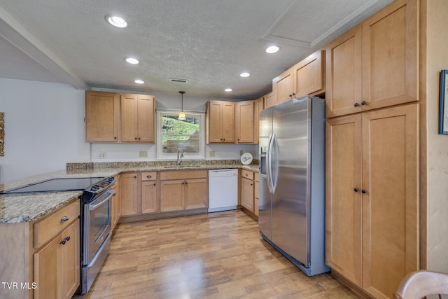 kitchen with light wood finished floors, a peninsula, stainless steel appliances, a textured ceiling, and a sink