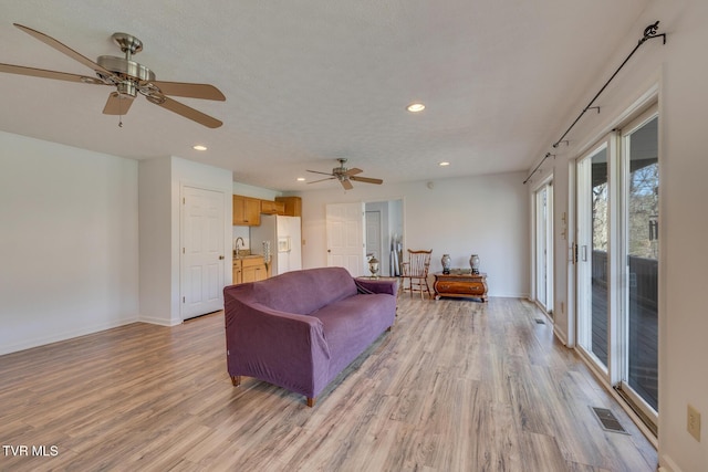 living area with light wood-type flooring, visible vents, a textured ceiling, and recessed lighting