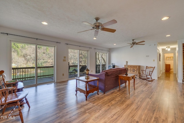 living room featuring recessed lighting, baseboards, light wood-style flooring, and a textured ceiling