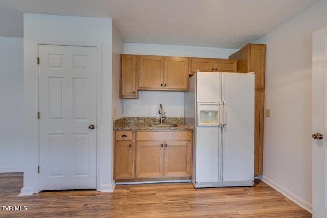 kitchen with stone counters, a sink, white fridge with ice dispenser, light wood-type flooring, and baseboards