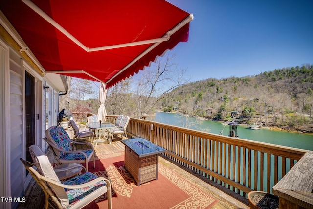 balcony with an outdoor fire pit, a deck with water view, a sunroom, a forest view, and outdoor dining space