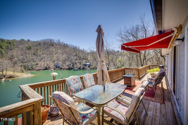 deck with outdoor dining area, a water view, and a wooded view