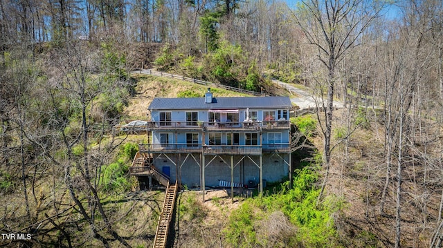 back of property featuring a chimney, stairway, metal roof, and a view of trees