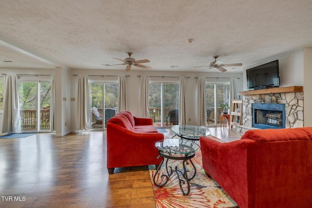 living room featuring plenty of natural light, a textured ceiling, wood finished floors, and a stone fireplace