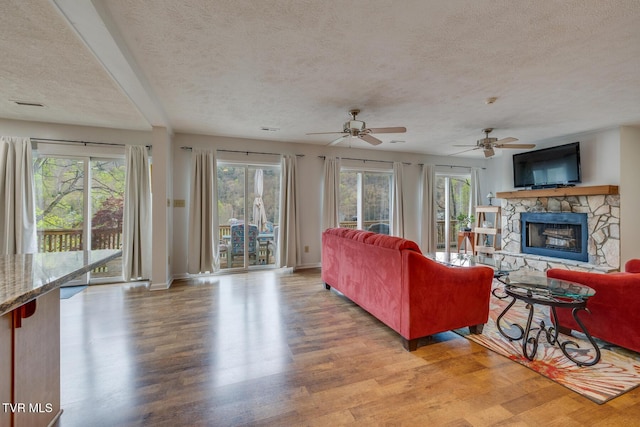 living area featuring light wood-type flooring, visible vents, a stone fireplace, and a textured ceiling