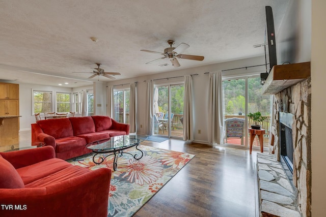 living room featuring a fireplace, a textured ceiling, baseboards, and wood finished floors