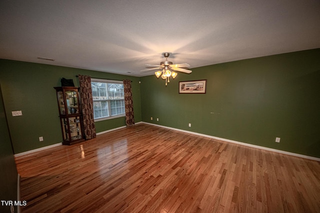 unfurnished room with ceiling fan, wood finished floors, visible vents, and baseboards