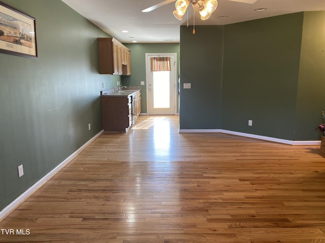 interior space featuring a ceiling fan, light wood-style flooring, baseboards, and a sink