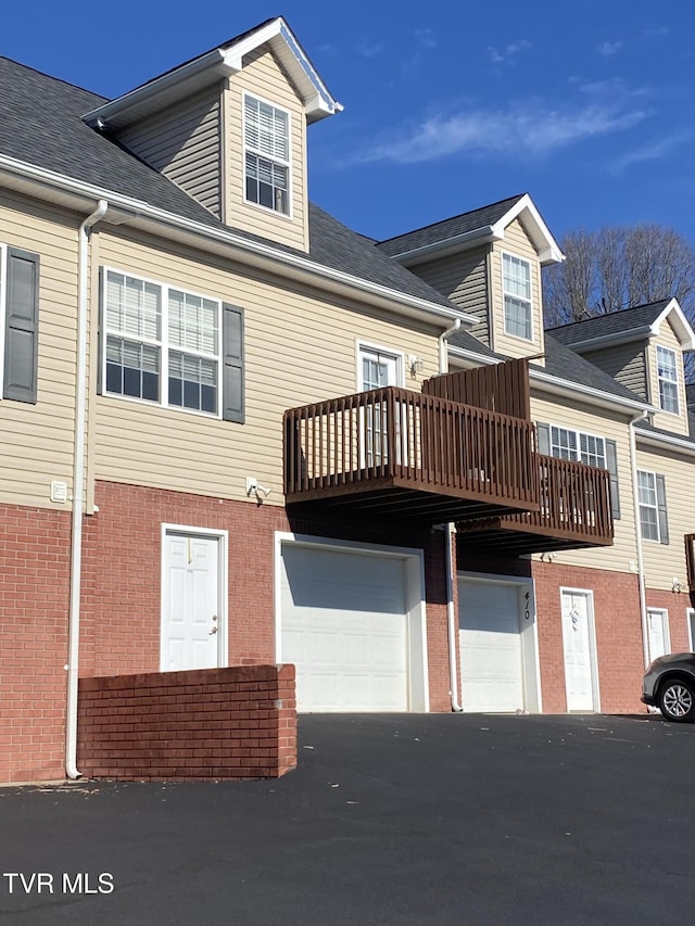 back of property featuring brick siding, driveway, an attached garage, and roof with shingles