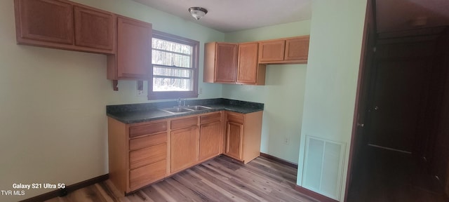 kitchen featuring a sink, visible vents, baseboards, light wood-style floors, and dark countertops