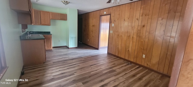 kitchen featuring dark countertops, ceiling fan, a sink, wooden walls, and wood finished floors