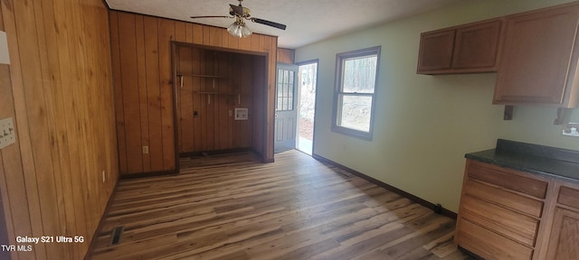 interior space featuring wooden walls, wood finished floors, a ceiling fan, brown cabinets, and dark countertops