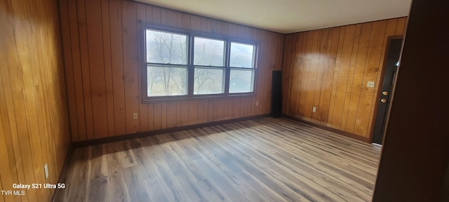 spare room featuring wood walls, baseboards, and wood finished floors