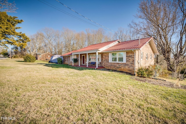 ranch-style home with covered porch, metal roof, brick siding, and a front yard