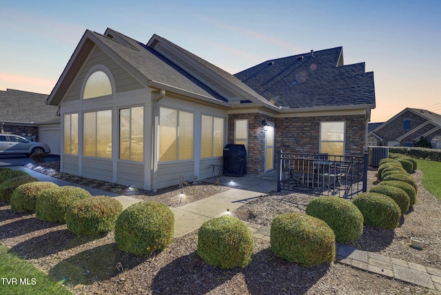 view of front of property with a shingled roof, cooling unit, a sunroom, and stone siding