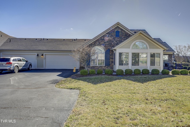 ranch-style home with a garage, stone siding, aphalt driveway, roof with shingles, and a front lawn