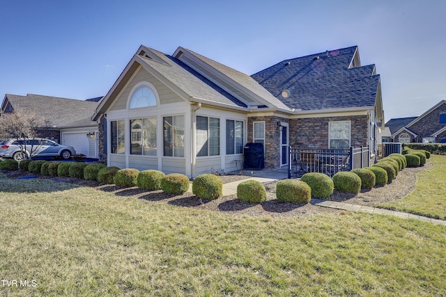 back of property featuring stone siding, a shingled roof, and a lawn