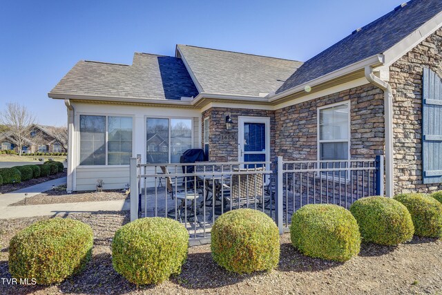 view of exterior entry with a shingled roof, stone siding, and a patio