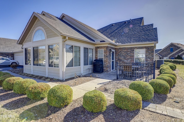 view of front of house with a shingled roof, a sunroom, a patio, and stone siding