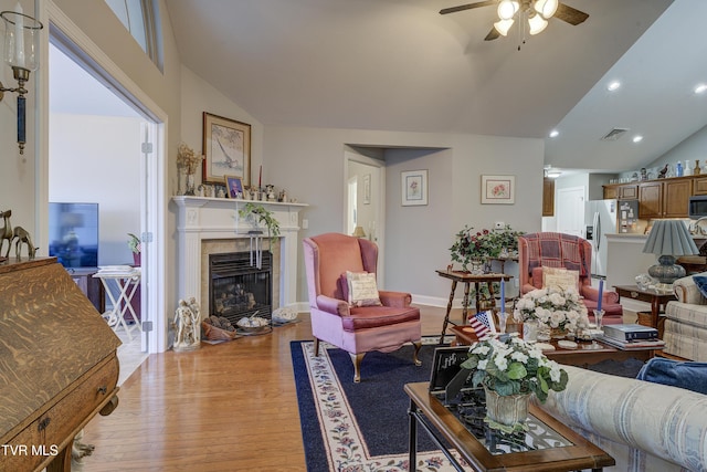 living room with lofted ceiling, light wood finished floors, a tiled fireplace, and visible vents