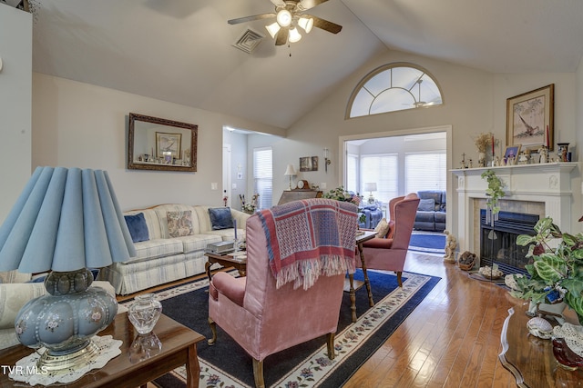 living room featuring ceiling fan, hardwood / wood-style flooring, visible vents, vaulted ceiling, and a tiled fireplace