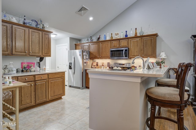 kitchen with a sink, a kitchen breakfast bar, light countertops, appliances with stainless steel finishes, and brown cabinets