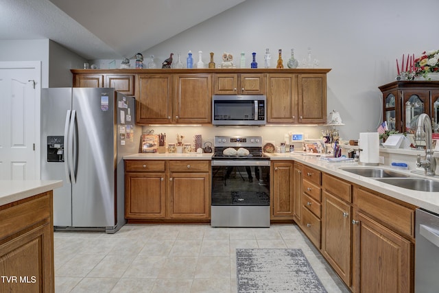 kitchen featuring lofted ceiling, light countertops, appliances with stainless steel finishes, brown cabinetry, and a sink