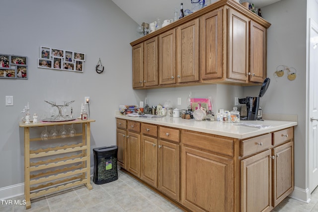 kitchen with brown cabinetry, light countertops, vaulted ceiling, and baseboards