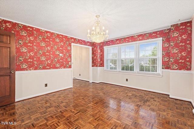 unfurnished room featuring wallpapered walls, a chandelier, a textured ceiling, and wainscoting