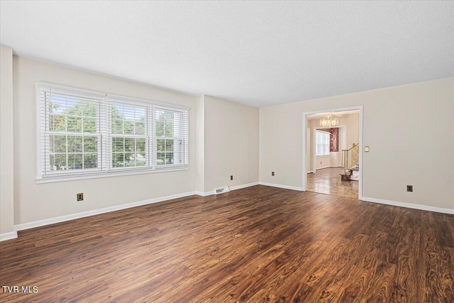 spare room with a textured ceiling, dark wood-type flooring, visible vents, baseboards, and an inviting chandelier