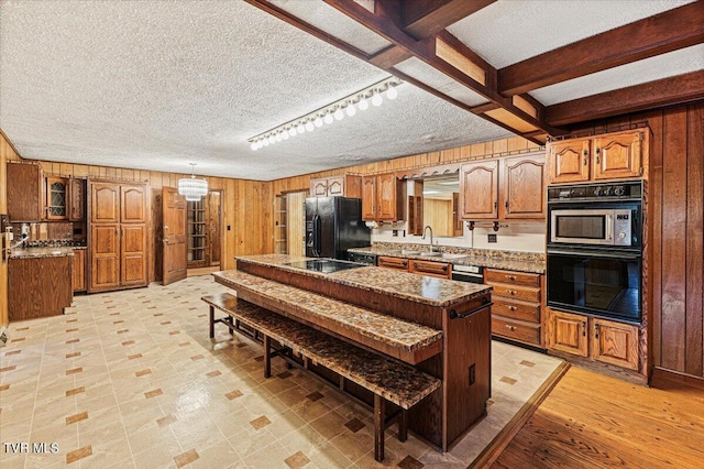 kitchen featuring a textured ceiling, black appliances, brown cabinetry, and wooden walls