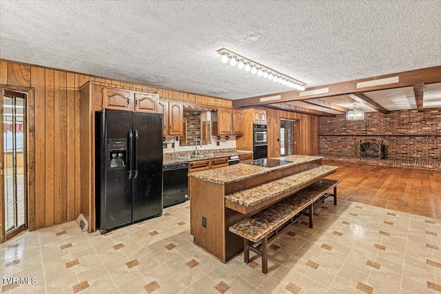 kitchen featuring a kitchen bar, a brick fireplace, wood walls, and black appliances