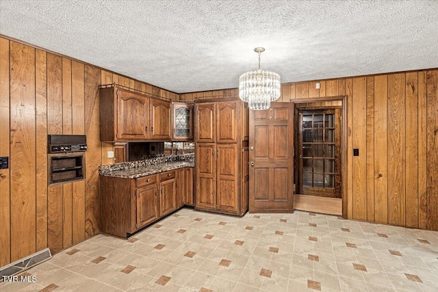 kitchen with a chandelier, brown cabinets, wooden walls, and a textured ceiling