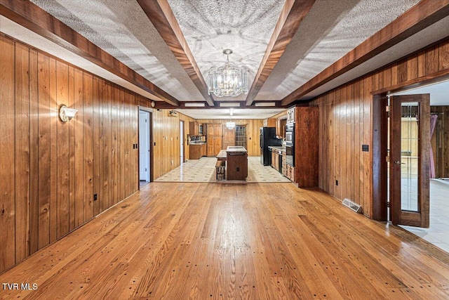 interior space with visible vents, light wood-style flooring, wood walls, a chandelier, and beamed ceiling