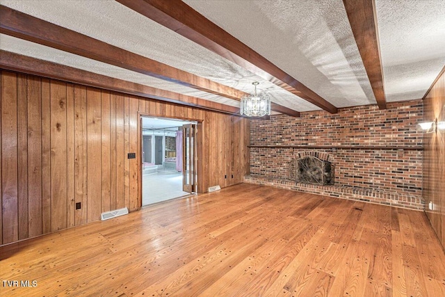 unfurnished living room featuring a textured ceiling, beam ceiling, a brick fireplace, and visible vents