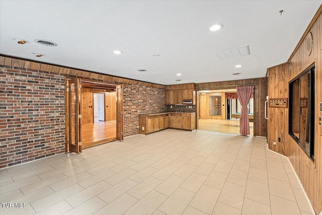 unfurnished living room featuring recessed lighting, visible vents, wooden walls, and brick wall