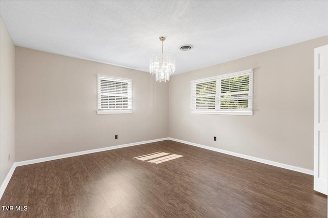 unfurnished room featuring dark wood finished floors, visible vents, an inviting chandelier, a textured ceiling, and baseboards