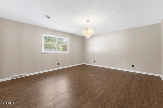 spare room featuring baseboards, visible vents, dark wood finished floors, and a chandelier