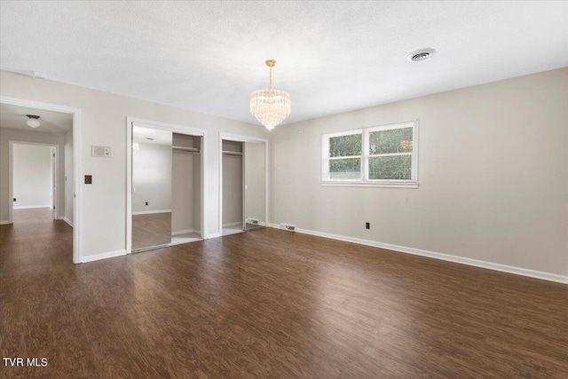 unfurnished bedroom featuring dark wood-style flooring, visible vents, baseboards, and two closets