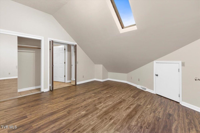 additional living space with vaulted ceiling with skylight, baseboards, and wood finished floors