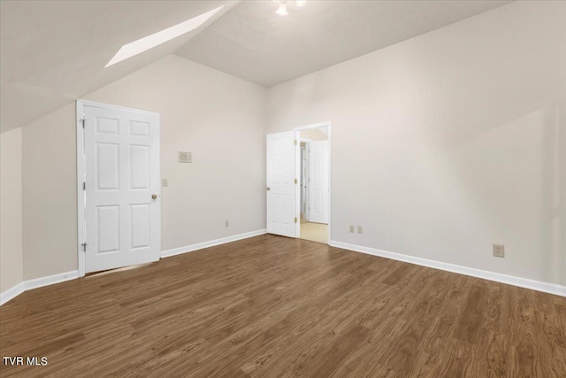 unfurnished bedroom with lofted ceiling with skylight, wood finished floors, and baseboards