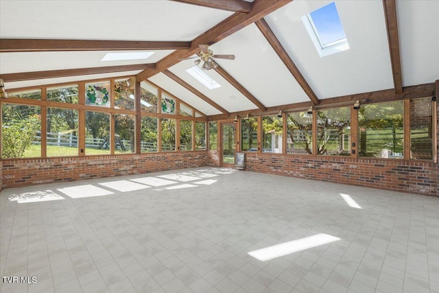 unfurnished living room with a skylight, plenty of natural light, a ceiling fan, brick wall, and beam ceiling