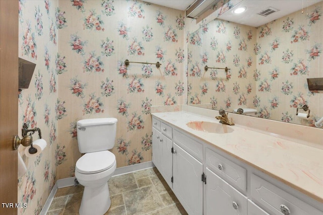 bathroom featuring visible vents, toilet, vanity, baseboards, and wallpapered walls