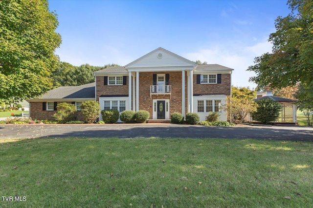 greek revival inspired property featuring a front yard, brick siding, and a balcony