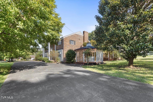 view of front facade with brick siding, a front yard, a chimney, and a gazebo